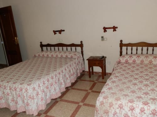 Habitación doble en Hostal San Poul de Consuegra con dos camas, cabeceros de madera, ropa de cama floral rosa y suelo de baldosa.