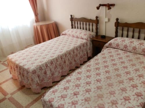 Habitación triple en Hostal San Poul de Consuegra con dos camas gemelas, edredones florales, cabeceros de madera y cortinas rosas