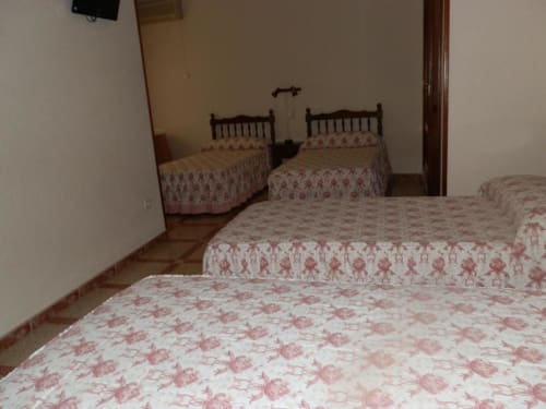 Habitación cuádruple del Hostal San Poul en Consuegra con cuatro camas de colchas florales rojas y suelo de baldosa