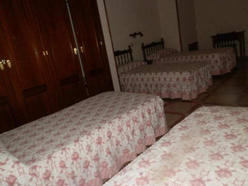 Habitación cuádruple en Hostal San Poul de Consuegra con múltiples camas, colchas rojas estampadas y armarios de madera