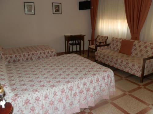 Habitación triple en Hostal San Poul de Consuegra con dos camas, ropa de cama floral, sofá, escritorio y TV
