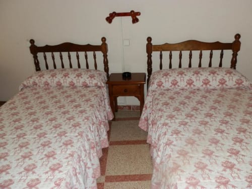 Dos camas individuales con colchas florales rosas y cabeceros de madera en el Hostal San Poul de Consuegra, España