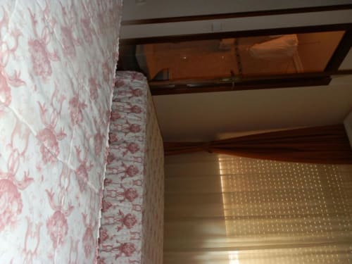 Acogedor dormitorio doble en Hostal San Poul de Consuegra con ropa de cama floral rosa, vigas de madera y vistas a la ciudad desde el balcón.