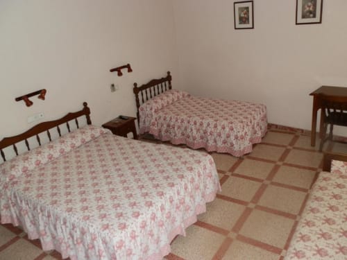 Habitación triple en Hostal San Poul de Consuegra con tres camas, muebles de madera, ropa de cama roja y blanca, y piso de baldosas.