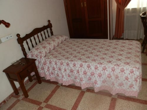 Habitación individual en el Hostal San Poul de Consuegra con cama de madera, ropa de cama floral, mesita de noche y piso de baldosas