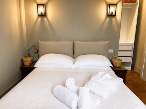 Tuscan Townhouse Garden Suite bedroom with white bedding, gray headboard, twin nightstands, wicker baskets, and ambient wall