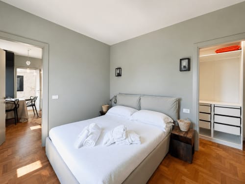 Modern bedroom in Tuscan Townhouse Garden Suite with queen bed, gray headboard, wooden floors, and open wardrobe in