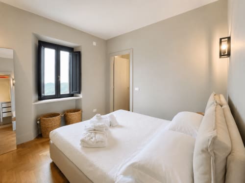 Bright bedroom with queen bed, white linens, black-framed window with garden view, and wooden floors at Tuscan Townhouse
