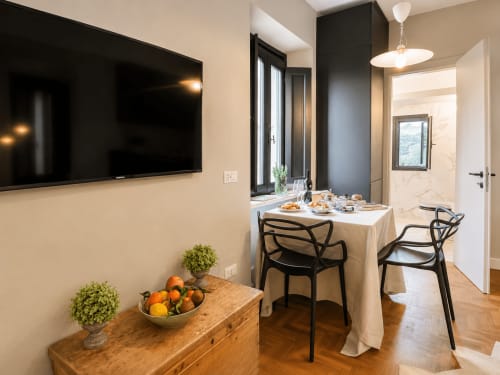 Modern dining area in Garden Suite at Tuscan Townhouse with flat-screen TV, round table, and black chairs overlooking garden