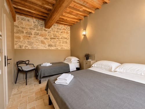 Tuscan townhouse twin bedroom with exposed wooden beams, stone walls, terracotta floors, and white linens at Montemassi hotel