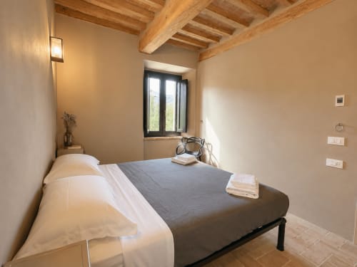 Tuscan bedroom in Montemassi with exposed wooden beams, queen bed, and window overlooking countryside