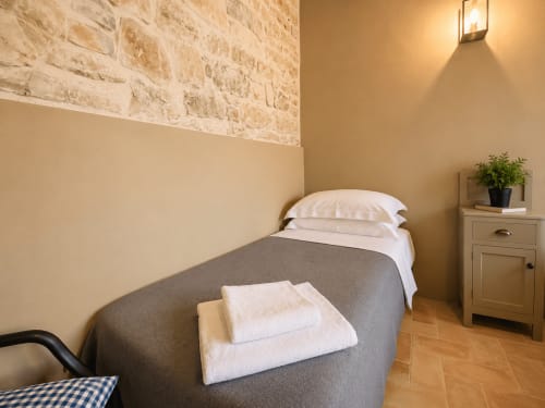 Tuscan townhouse bedroom with stone accent wall, queen bed, white pillows, gray throw blanket, wooden nightstand with potted