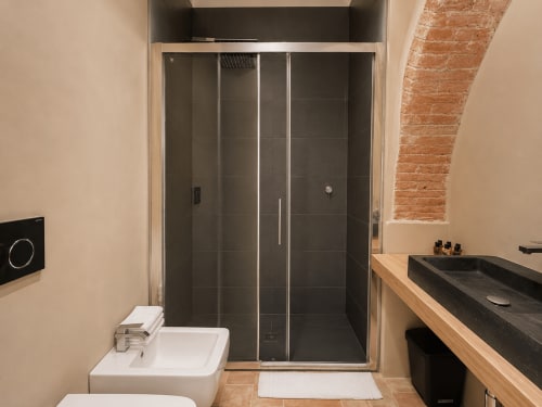 Modern bathroom in Tuscan townhouse with rainfall shower, dark tiled enclosure, and wooden vanity