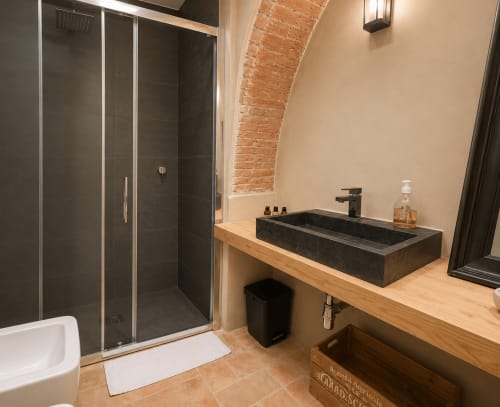 Modern bathroom in Tuscan Townhouse with black vessel sink, walk-in shower, and exposed brick architecture in Montemassi