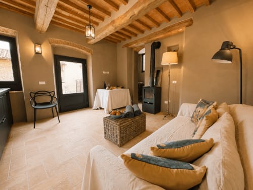 Tuscan townhouse apartment with exposed wooden beams, cream sofa, fireplace, and rustic décor in Montemassi, Italy