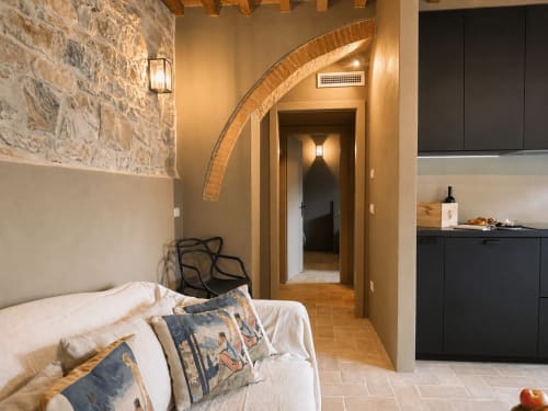 Tuscan townhouse studio with exposed stone walls, brick archway, bed, and kitchenette in Montemassi, Italy