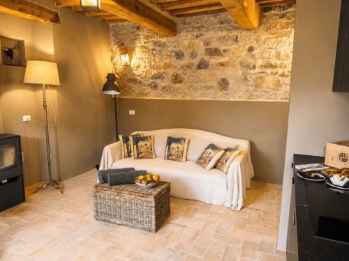 Tuscan Townhouse Club apartment in Montemassi with stone walls, wooden beams, cream sofa, and warm lighting