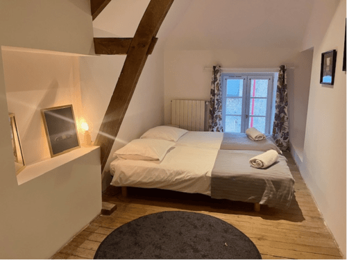 Chambre douillette du Château de Moulins avec poutres en bois, lit double et vue sur le jardin