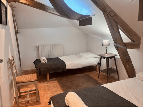 Chambre rustique au Château de Moulins avec poutres apparentes, lit aux draps blancs et sol en terre cuite