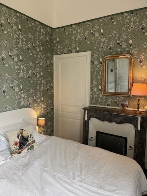 Elegant bedroom at Chateau de Moulins with floral wallpaper, white bed, black fireplace, and gold-framed mirror