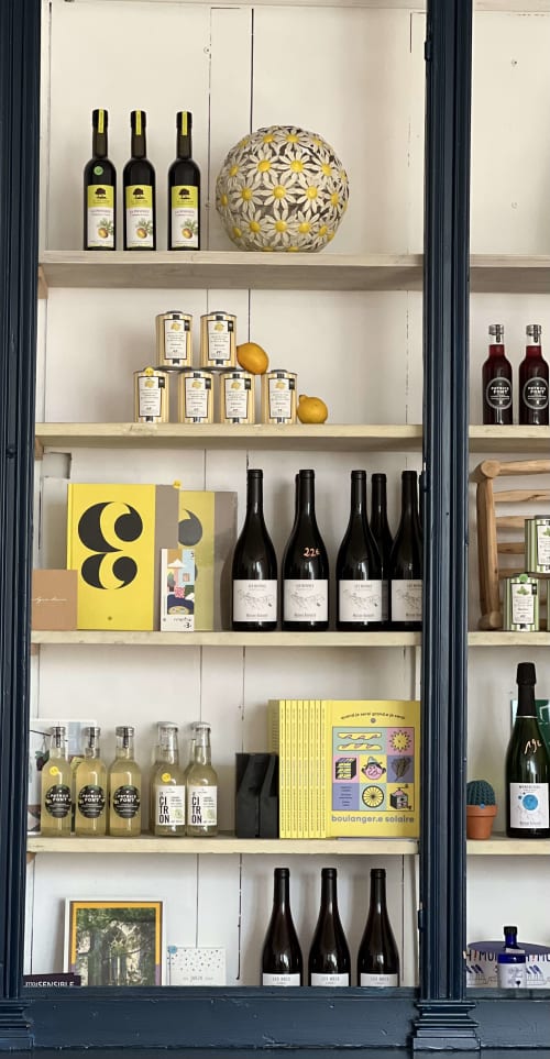 Vitrine curatée à La Maison d'Ambronay présentant bouteilles de vin, produits gastronomiques et objets décoratifs sur fond blanc