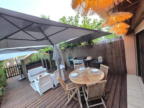 Spacieuse terrasse à La Montagnette à Cap d'Agde avec table de dining en bois, chaises longues et parasol gris