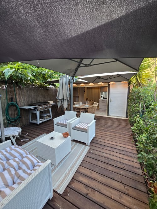 Patio de l'appartement-jardin La Montagnette avec coin détente ombragé, chaises longues blanches, espace repas et barbecue à Cap d'Agde