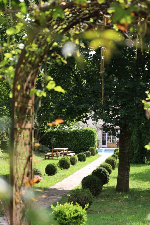 Allée verdoyante du Domaine Chapelle B&B avec arche couverte de lierre, haies taillées et bâtisse en pierre