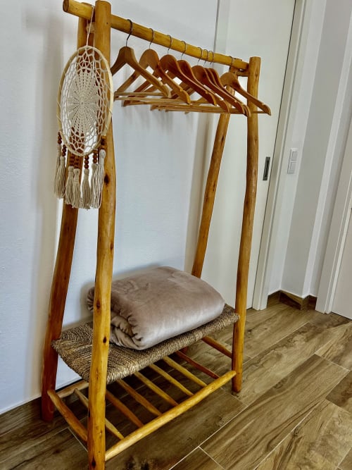 Cabideiro de madeira com apanhador de sonhos branco e almofada bege no quarto do hotel Ocean House Alentejo
