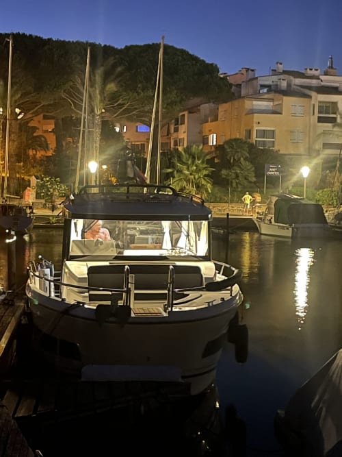 Yacht de luxe amarré à la marina de Cap d'Agde la nuit, bâtiments illuminés et palmiers en arrière-plan