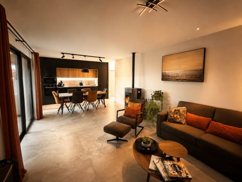 Séjour contemporain à la Villa Cinto, Corse : canapé sombre, tables en bois, cuisine ouverte aux armoires noires
