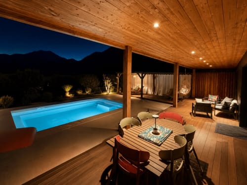Villa de luxe en Corse la nuit avec piscine chauffée illuminée, terrasse en bois pour dîner et vue sur les montagnes sous un ciel étoilé