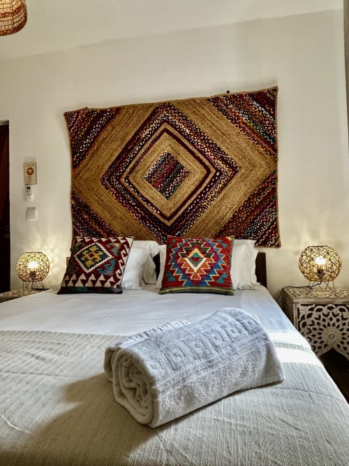 Quarto boho na Ocean House Alentejo com tapeçaria geométrica, almofadas kilim coloridas, luminárias globo trançadas e