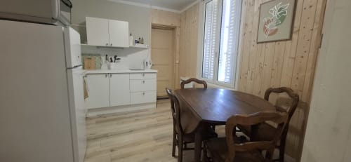 Cuisine-salle à manger de l'appartement Accolade à Châteaudun avec armoires blanches, table en bois et murs en pin