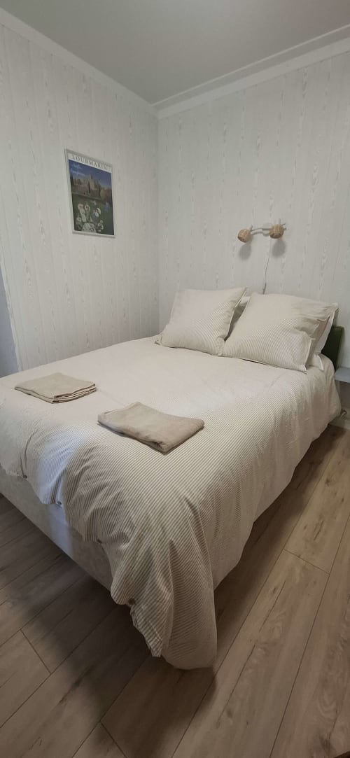 Chambre minimaliste à l'appartement Accolade à Châteaudun avec literie crème, oreillers rayés, parquet et cadre mural
