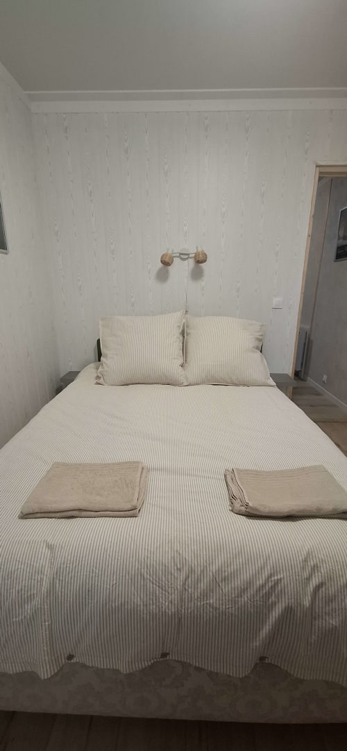 Chambre accueillante à l'Accolade Châteaudun avec literie rayée neutre, oreillers, serviettes pliées et applique murale décorative