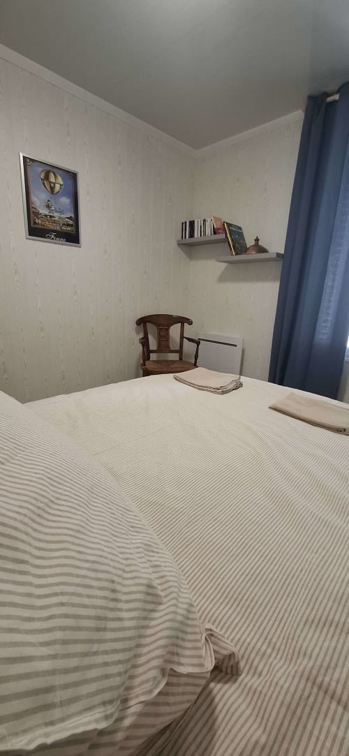 Chambre cosy à l'Accolade Châteaudun avec literie rayée, chaise en bois, étagères murales et rideaux bleus
