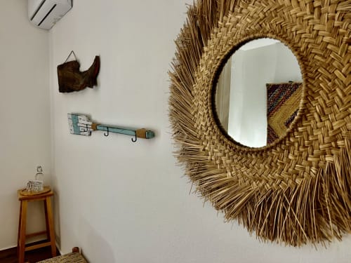 Decoração do quarto de hotel costeiro com espelho de palha trançada, ornamento de peixe em madeira e ganchos turquesas na parede da Ocean House Alentejo