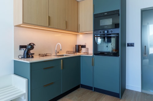 Modern kitchen with teal cabinets, light wood upper units, and stainless steel appliances at Suites Avenue Lux Apartments,