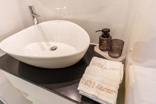 Modern bathroom sink at Suites Avenue Lux Apartments in Horta with white vessel basin, black countertop, and branded towels