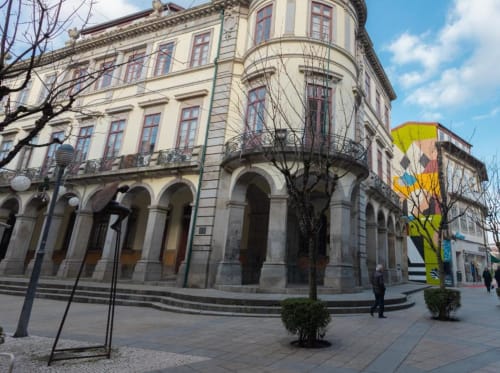 Fachada histórica em Braga, Portugal com colunatas em arco, varandas e arte de rua colorida nas proximidades