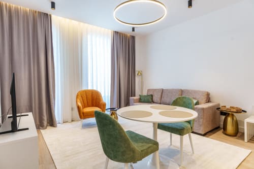 Modern studio at Suites Avenue Lux Apartments in Horta with dining table, green chairs, orange armchair, and sofa