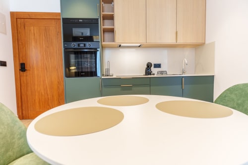 Modern kitchen with green and wood cabinetry, white round table at Suites Avenue Lux Apartments, Horta