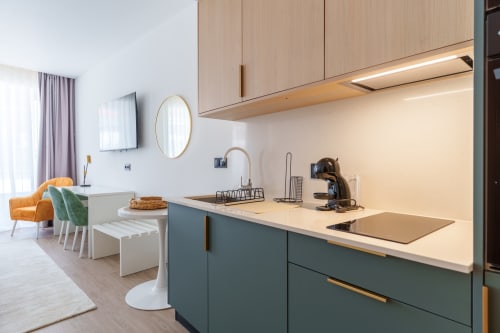 Modern kitchenette with teal cabinets, light wood upper units, and cream countertops at Suites Avenue Lux Apartments, Horta