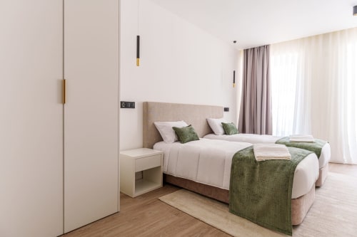Modern hotel suite bedroom at Suites Avenue Lux with twin beds, beige headboard, green accents, and natural light from patio