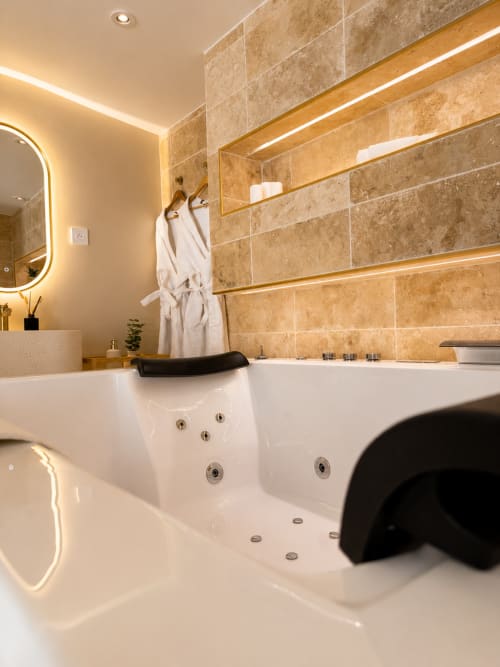 Salle de bains luxueuse à l'hôtel L'Escapade au Mans avec baignoire spa, carrelage en travertin et accents dorés