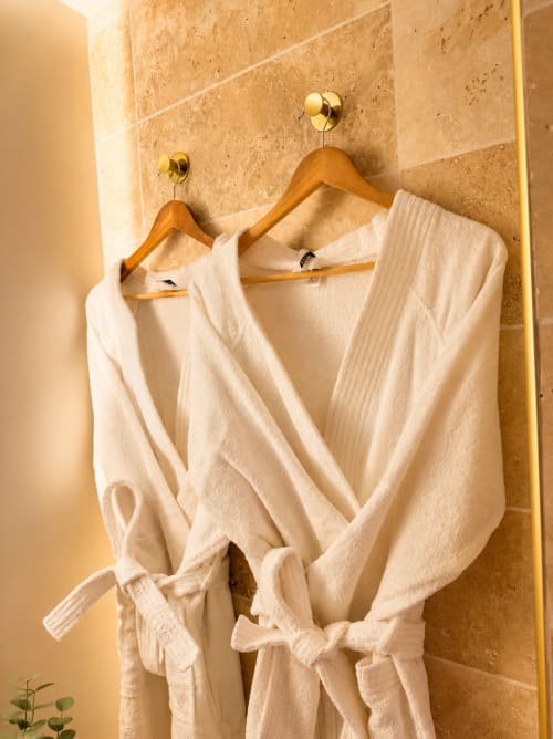Robes de couleur crème suspendues à des cintres en bois avec crochets en laiton dans la salle de bains en travertin de l'hôtel L'Escapade, Le Mans