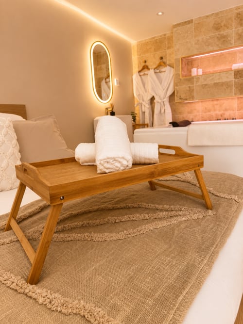 Chambre luxueuse à L'Escapade Le Mans avec banc en bois, serviettes blanches et miroir ovale lumineux