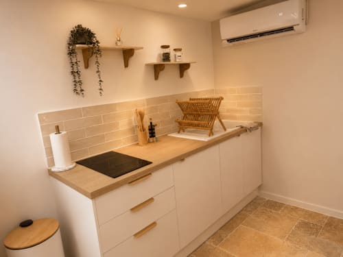 Kitchenette moderne à l'hôtel L'Escapade au Mans avec meubles blancs, plan de travail en bois et carrelage beige