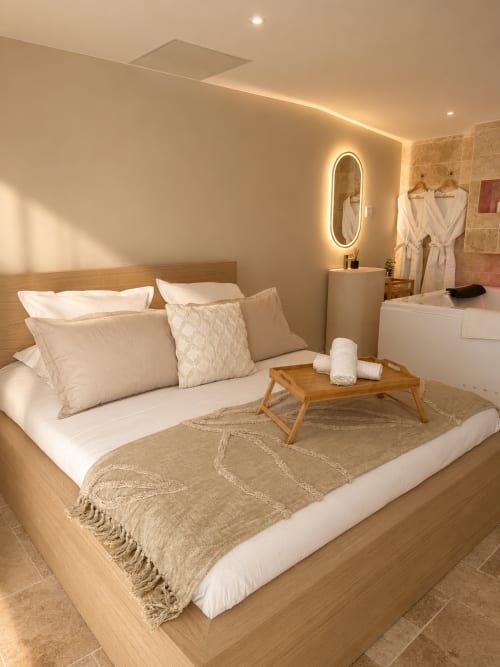 Chambre de luxe à l'hôtel L'Escapade au Mans avec lit en bois, éclairage ambiant et salle de bain style spa